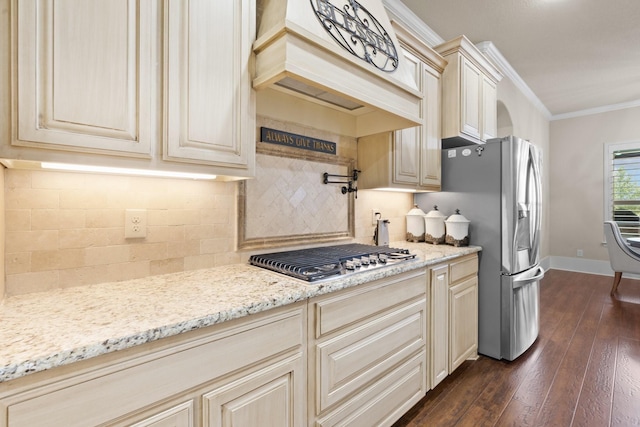 kitchen with light stone counters, cream cabinetry, appliances with stainless steel finishes, ornamental molding, and premium range hood