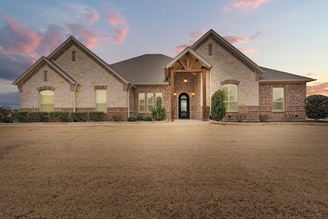 french country home featuring a shingled roof and brick siding