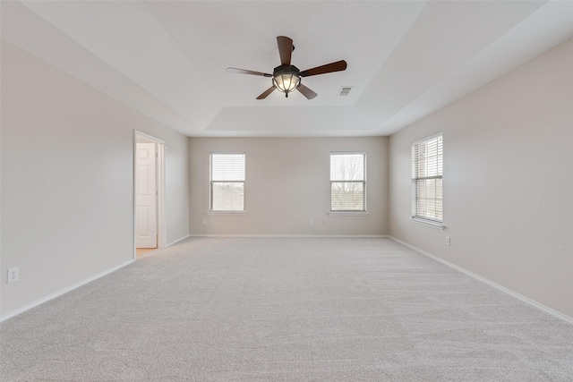 carpeted spare room featuring ceiling fan, plenty of natural light, and a raised ceiling