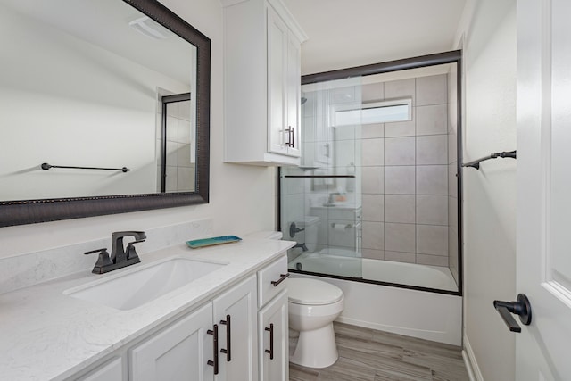 full bathroom with vanity, wood-type flooring, bath / shower combo with glass door, and toilet