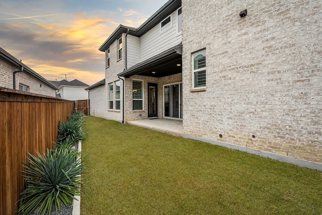 back house at dusk with a lawn and a patio area