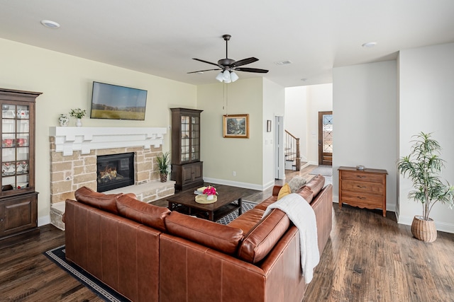 living room featuring a stone fireplace, dark wood-type flooring, and ceiling fan