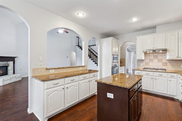 kitchen with light stone countertops, kitchen peninsula, white cabinets, and appliances with stainless steel finishes