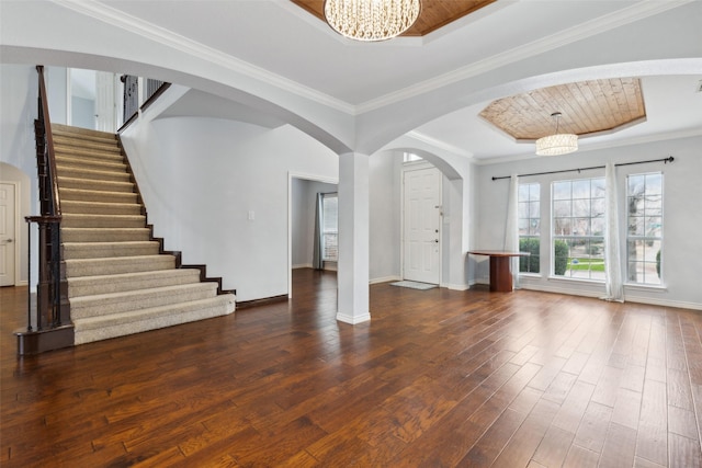 unfurnished living room with ornamental molding, dark wood-type flooring, a notable chandelier, and a tray ceiling