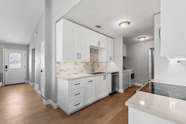 kitchen with appliances with stainless steel finishes, sink, white cabinets, washing machine and clothes dryer, and light hardwood / wood-style floors