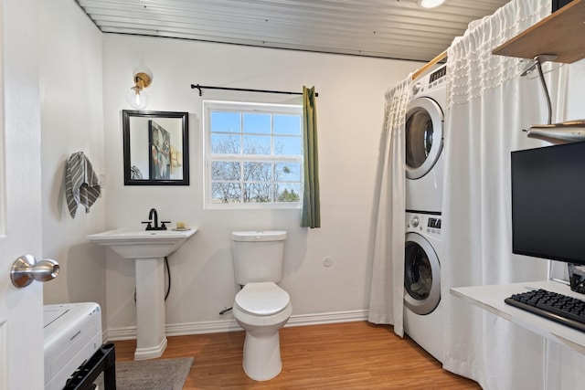 bathroom with hardwood / wood-style flooring, stacked washer and clothes dryer, and toilet