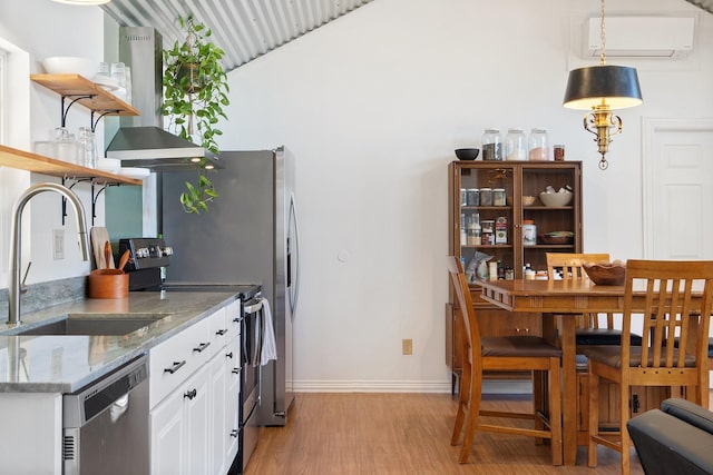 kitchen featuring pendant lighting, sink, appliances with stainless steel finishes, white cabinets, and wall chimney exhaust hood