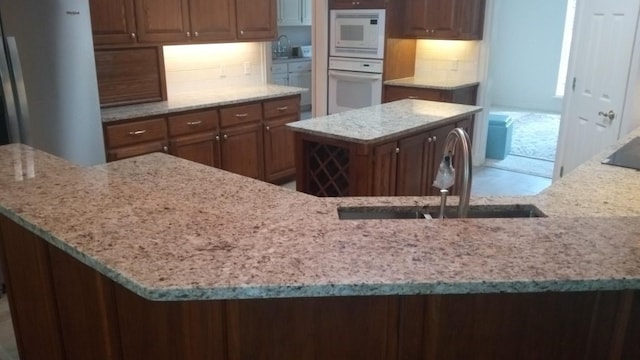 kitchen with sink, light stone counters, a kitchen island, white appliances, and decorative backsplash