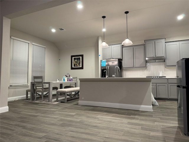 kitchen with pendant lighting, stainless steel fridge, gray cabinetry, stainless steel refrigerator with ice dispenser, and a center island with sink