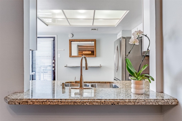 kitchen featuring light stone counters, sink, and stainless steel fridge