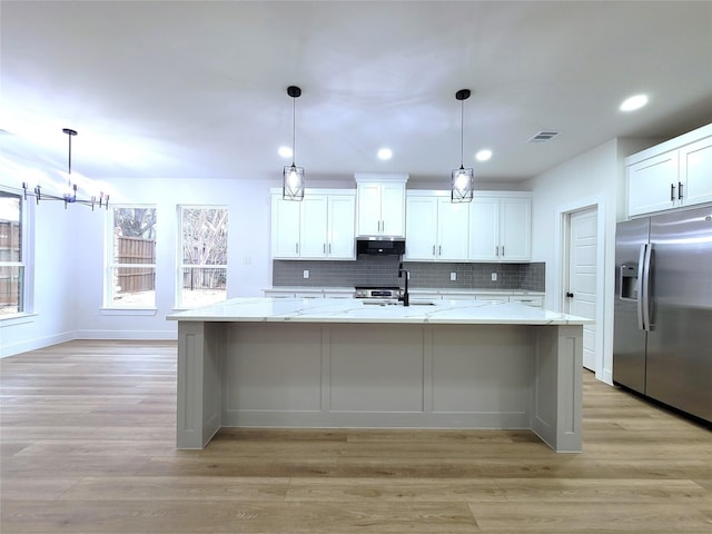 kitchen featuring hanging light fixtures, stainless steel appliances, ventilation hood, an island with sink, and white cabinets