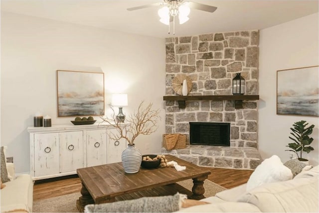 living room featuring ceiling fan, a stone fireplace, and light hardwood / wood-style floors