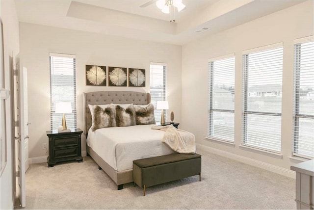 carpeted bedroom with multiple windows, a raised ceiling, and ceiling fan