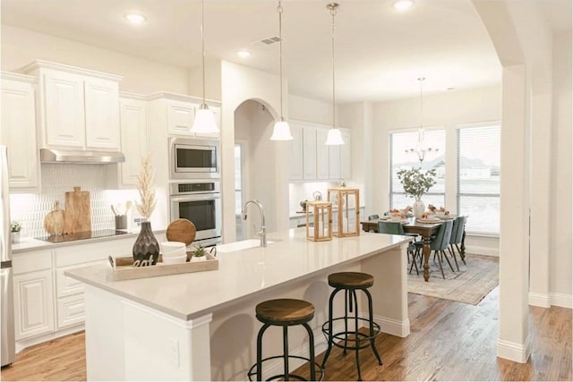 kitchen with a large island with sink, appliances with stainless steel finishes, white cabinets, and decorative light fixtures