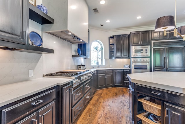 kitchen with island range hood, sink, built in appliances, crown molding, and dark wood-type flooring