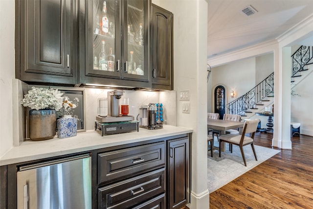 bar with dark wood-type flooring, dark brown cabinetry, crown molding, stainless steel fridge, and backsplash