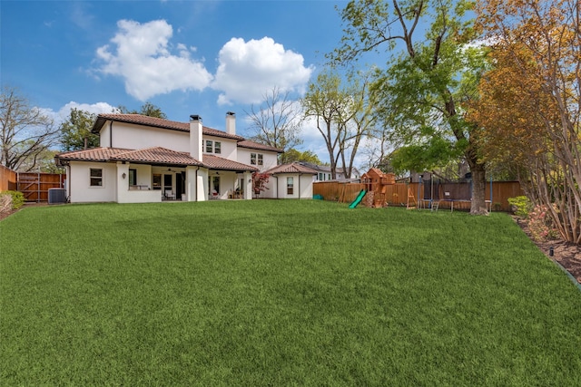 rear view of property featuring a playground, central AC, a trampoline, and a lawn