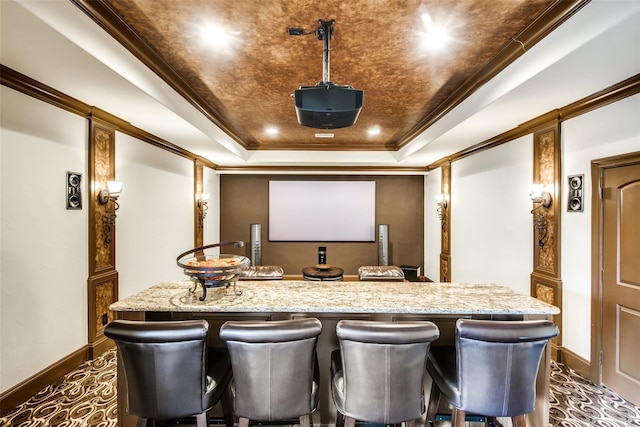 cinema room with a raised ceiling, crown molding, and bar area