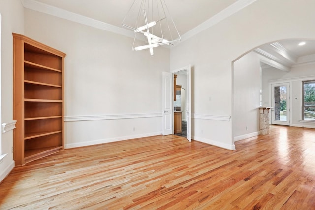 spare room featuring arched walkways, crown molding, and light wood-style flooring