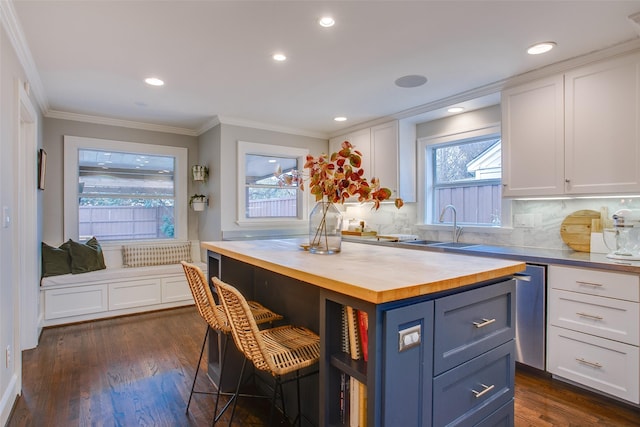 kitchen featuring a kitchen island, dark hardwood / wood-style floors, butcher block countertops, white cabinetry, and a breakfast bar area