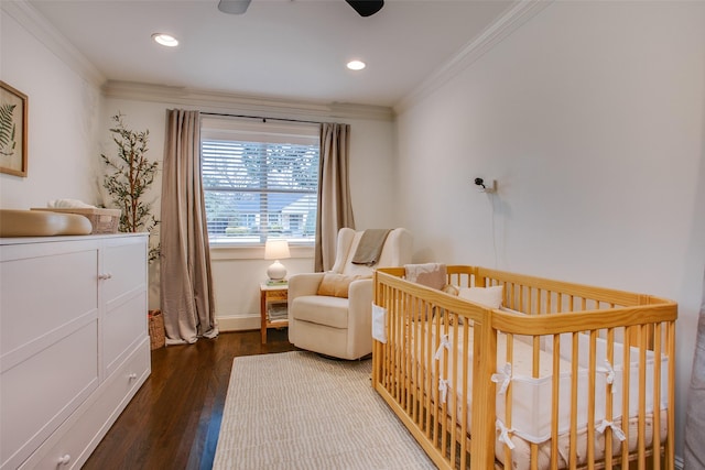 bedroom with crown molding, ceiling fan, a nursery area, and dark hardwood / wood-style flooring