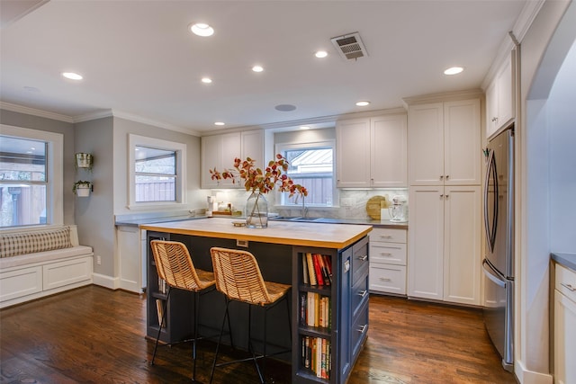 kitchen with dark wood-type flooring, wood counters, a breakfast bar, a kitchen island, and white cabinets