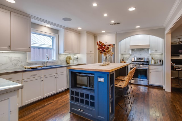 kitchen with wood counters, a breakfast bar, white cabinetry, a center island, and appliances with stainless steel finishes