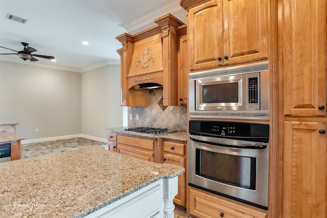 kitchen with light stone counters, ornamental molding, ceiling fan, stainless steel appliances, and backsplash