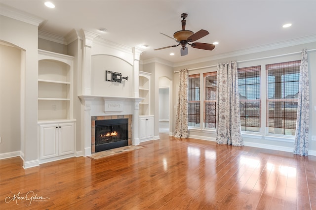 unfurnished living room featuring hardwood / wood-style flooring, a tile fireplace, ornamental molding, and built in shelves