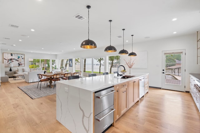 kitchen featuring pendant lighting, sink, a large island with sink, light hardwood / wood-style floors, and light stone countertops