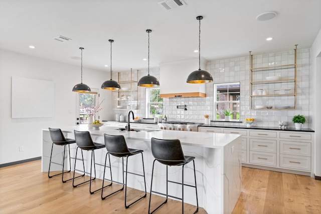 kitchen with white cabinetry, hanging light fixtures, sink, and a large island with sink