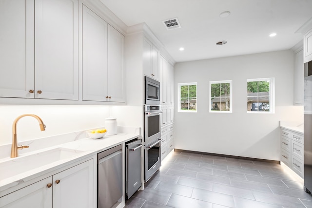 kitchen with stainless steel appliances, white cabinetry, sink, and light stone counters