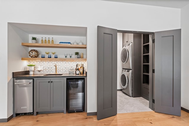 washroom featuring stacked washer / drying machine, indoor wet bar, beverage cooler, and light hardwood / wood-style flooring