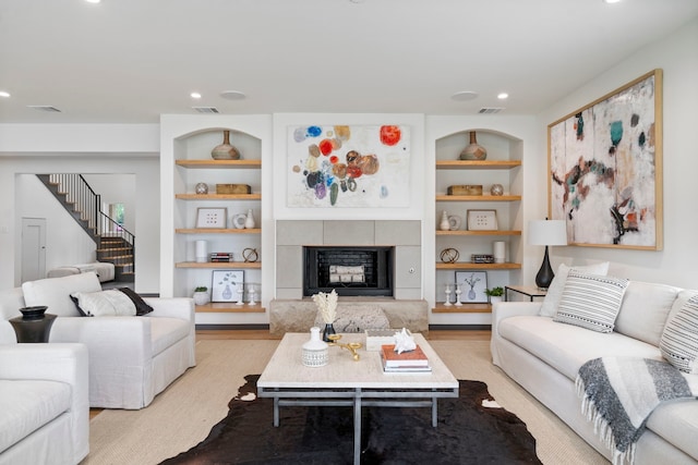 living room featuring built in shelves, a tile fireplace, and light hardwood / wood-style floors