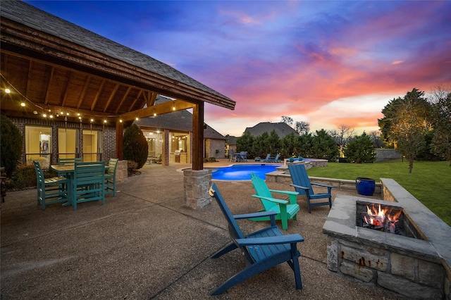 patio terrace at dusk featuring a fire pit and a lawn