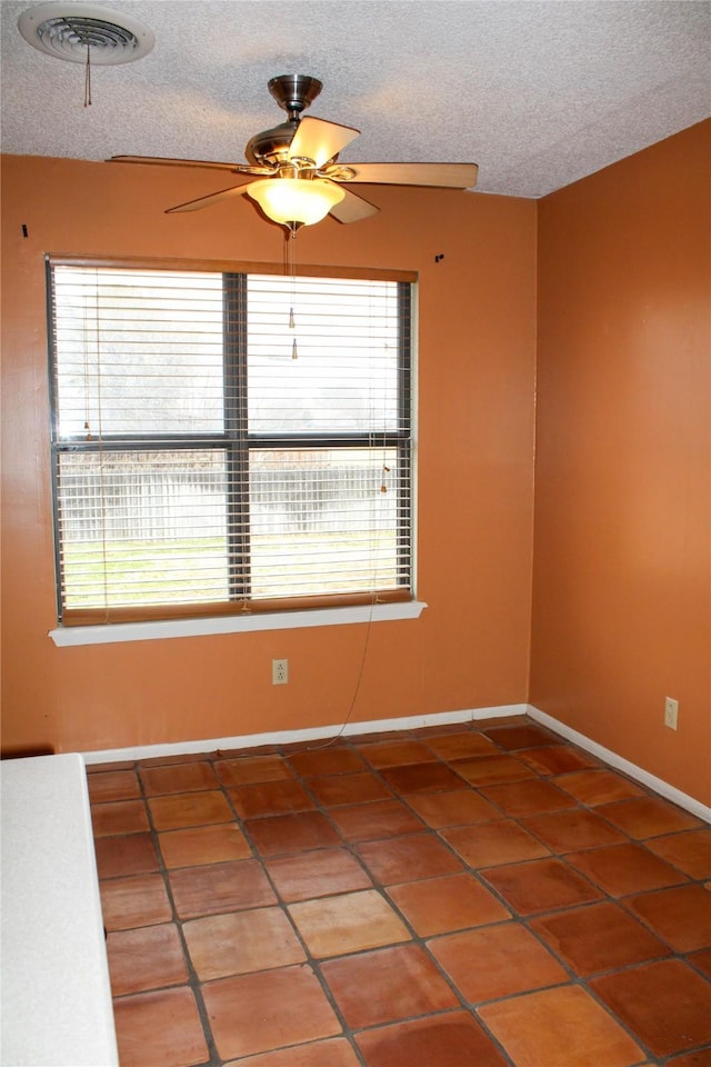 empty room featuring ceiling fan, a healthy amount of sunlight, tile patterned floors, and a textured ceiling