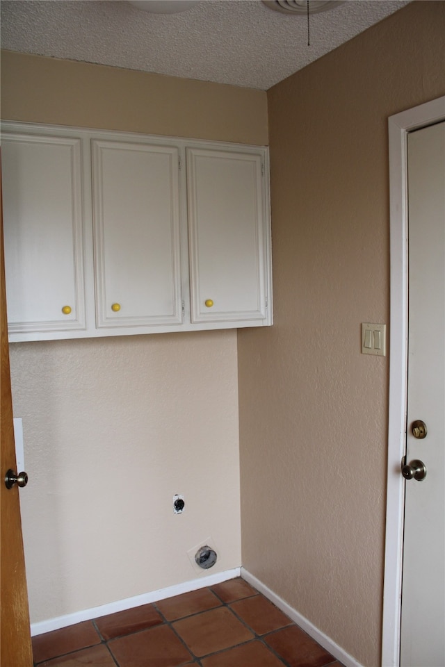 laundry room with cabinets, electric dryer hookup, dark tile patterned flooring, and a textured ceiling