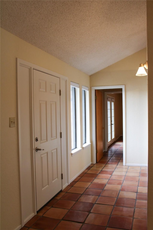 entrance foyer featuring dark tile patterned flooring, vaulted ceiling, and a textured ceiling