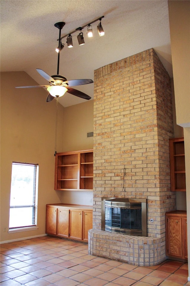 unfurnished living room featuring ceiling fan, light tile patterned floors, a fireplace, and a textured ceiling