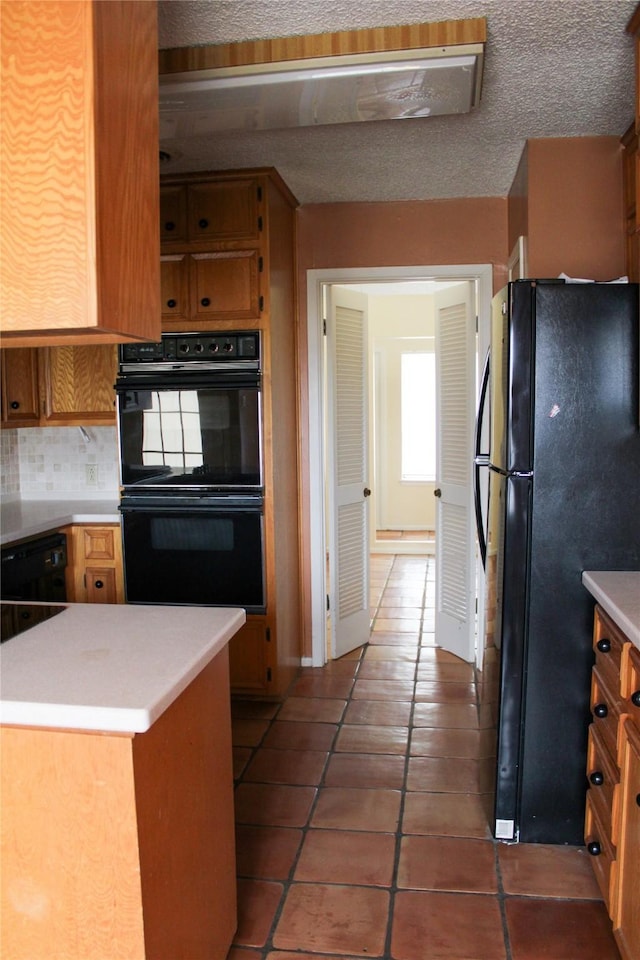 kitchen featuring a textured ceiling, kitchen peninsula, tile patterned flooring, decorative backsplash, and black appliances