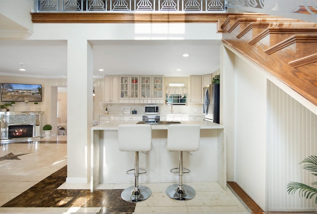 kitchen with appliances with stainless steel finishes, a breakfast bar, decorative backsplash, ornamental molding, and cream cabinets