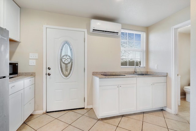 kitchen with light tile patterned floors, sink, a wall unit AC, and white cabinets