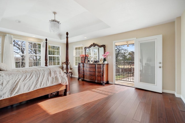 bedroom with dark hardwood / wood-style flooring, access to exterior, and a raised ceiling