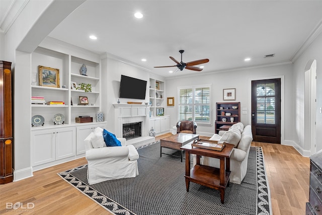 living room with crown molding, a fireplace, light hardwood / wood-style floors, and ceiling fan