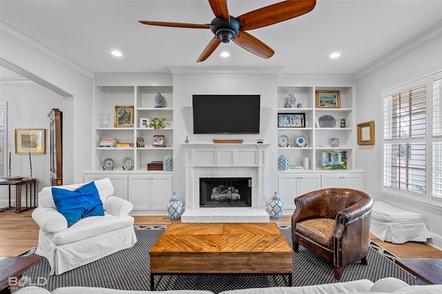 living room with crown molding, built in features, a fireplace, and light hardwood / wood-style flooring