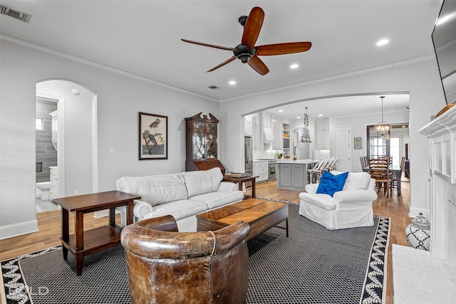 living room featuring crown molding, ceiling fan with notable chandelier, and light hardwood / wood-style flooring