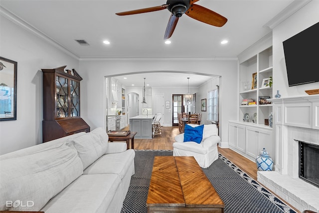 living room featuring ornamental molding, a fireplace, light wood-type flooring, and built in shelves