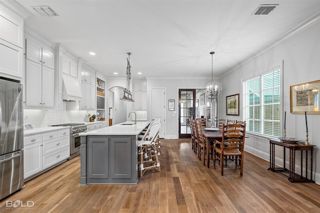 kitchen featuring stainless steel appliances, custom range hood, white cabinets, and a center island with sink