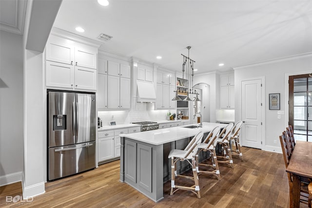 kitchen with a breakfast bar area, a kitchen island with sink, white cabinets, stainless steel fridge with ice dispenser, and decorative light fixtures