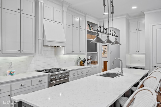 kitchen with sink, a kitchen island with sink, hanging light fixtures, high end stove, and custom exhaust hood